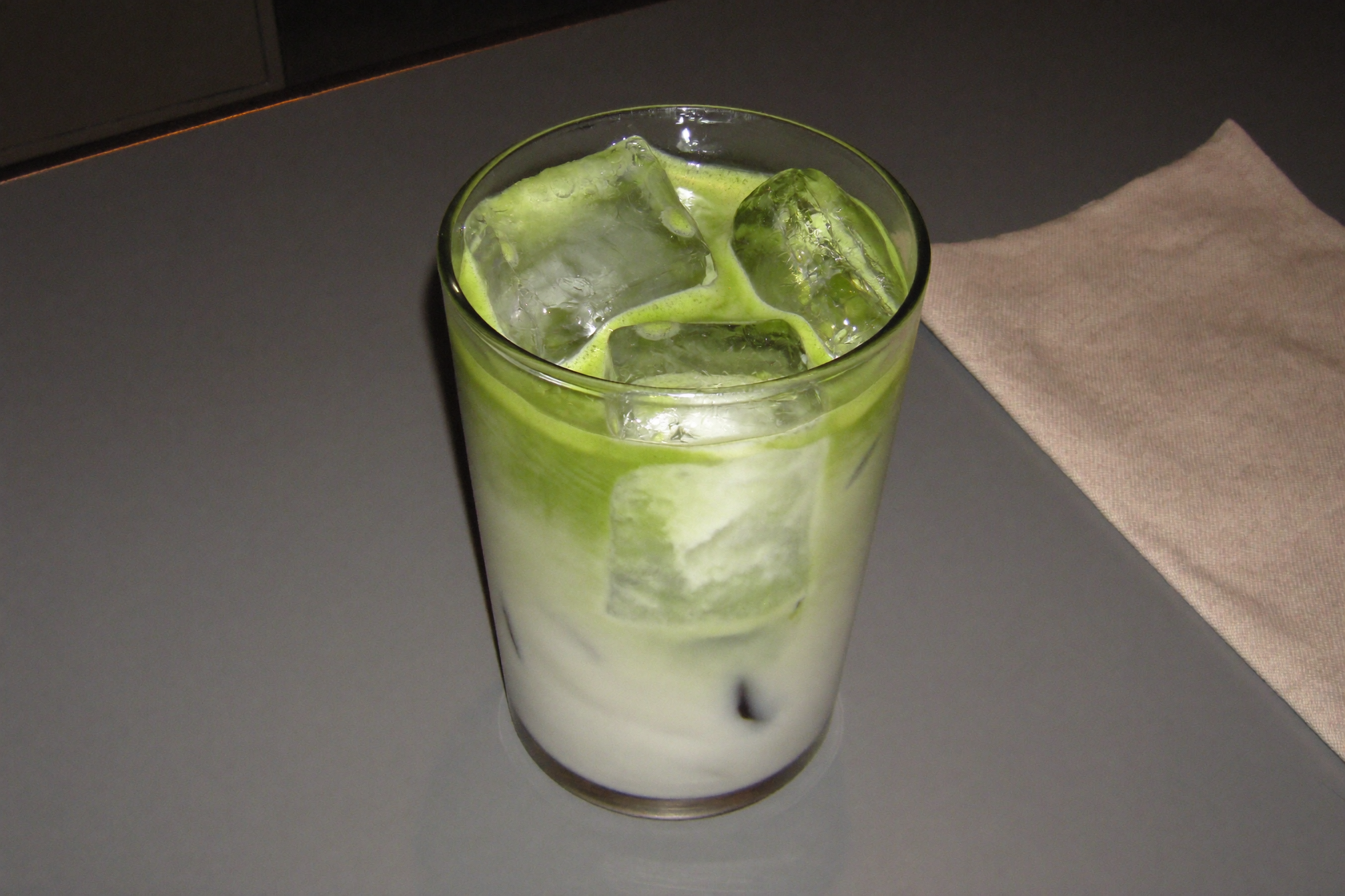 Iced matcha latte with ice cubes in a tall glass on a gray table