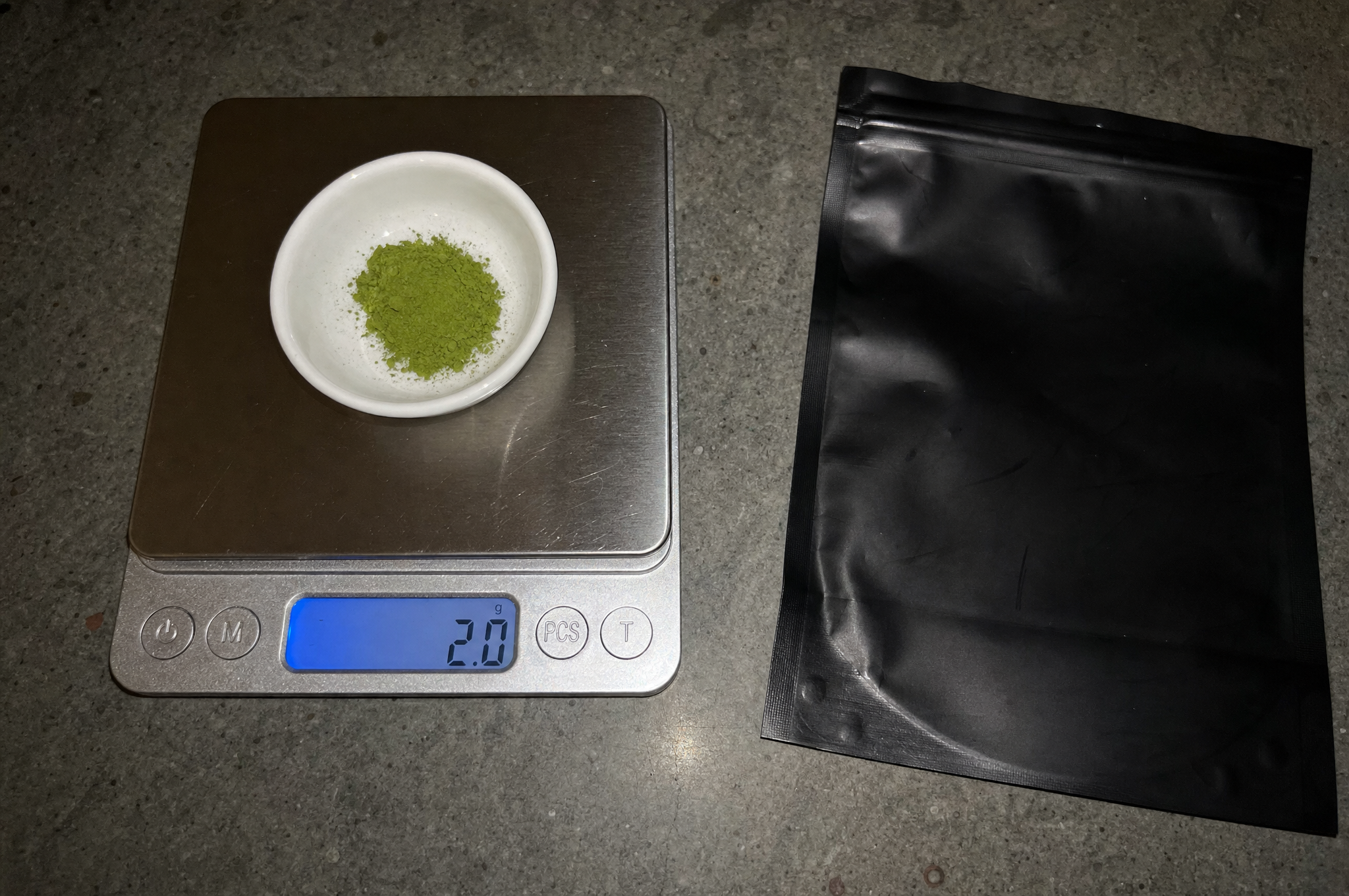 Kitchen scale weighing 2 grams of matcha powder next to a black pouch