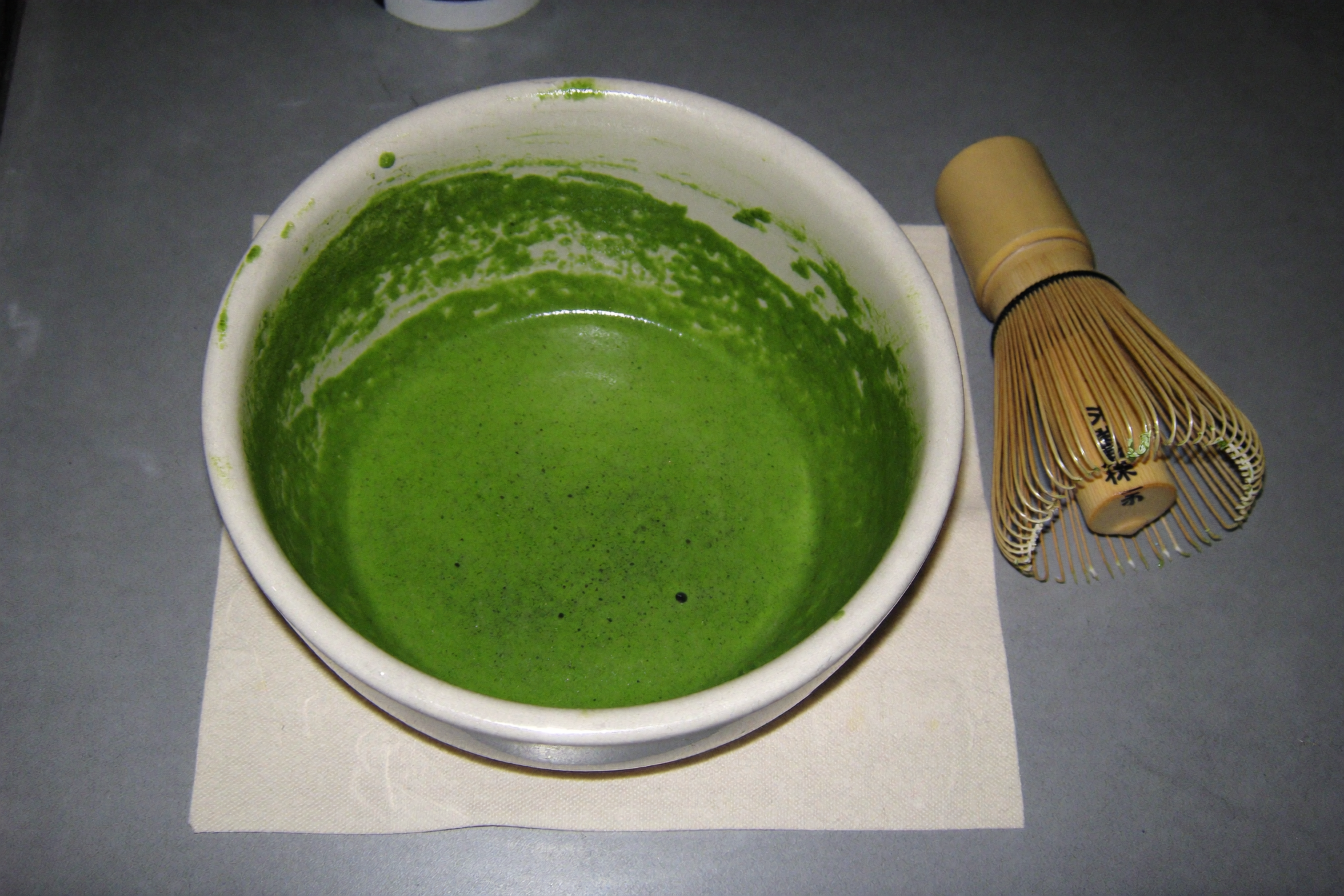 Bowl of freshly whisked ceremonial matcha with fine foam next to a bamboo whisk